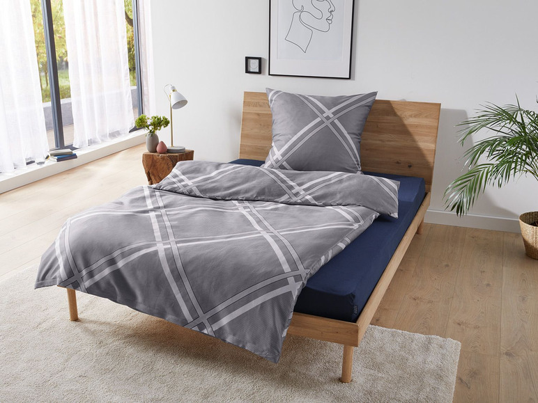 Graue Bettwäsche mit geometrischem Muster auf einem Holzbettgestell.