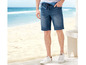 Mann trägt blaue Jeans-Shorts und weiße Sneaker am Strand.