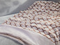 Eine weiche, beige Decke mit Schuppenmuster auf einer grauen Couch.