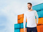 Mann mit einem weißen T-Shirt vor einem Stapel Container.