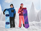 Zwei Kinder in Skibekleidung mit blauen und violetten Snowboards im Schnee.