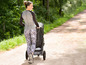 Eine Frau in Sportkleidung geht mit einem Kinderwagen durch einen Waldweg.