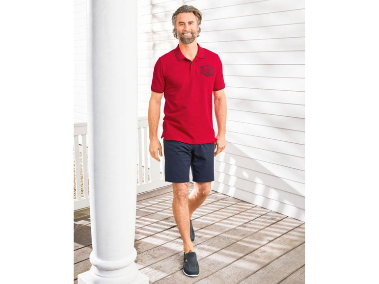 Mann in einem roten Poloshirt mit kurzen Ärmeln, blauen Shorts und schwarzen Schuhen.