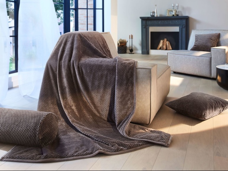 Eine braune Mikrofaser-Decke auf einem beigen Sessel mit passendem Kissen.