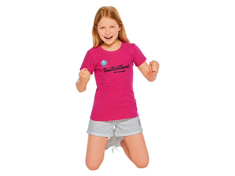 Ein Mädchen in einem rosafarbenen T-Shirt mit dem Aufdruck 'Deutschland' und grauen Shorts.