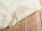 Ein weißer, flauschiger Teppich auf einem Holzboden.