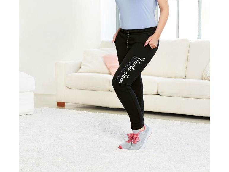 Frau in schwarzen Jogginghosen mit 'Just sayin' Aufdruck und rosafarbenen Sneakern.