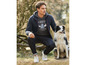Mann mit schwarzem Hoodie, Jeans und weißen Sneakern posiert mit einem Hund.