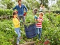 Kinder helfen im Garten mit einem zusammenklappbaren Abfalleimer.
