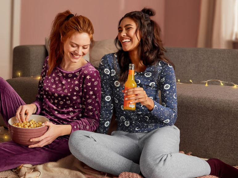 Zwei Frauen in Pyjamas mit Sternmuster entspannen auf dem Sofa mit Popcorn und einem Getränk.