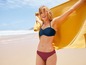 Eine Frau in einem blauen Bikini und einem gelben Handtuch am Strand.