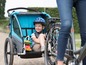 Ein Kind in einem blauen Fahrradanhänger, der von einem Fahrrad gezogen wird.