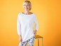 Eine Frau in einem weißen Pullover und einer Blumenhose.