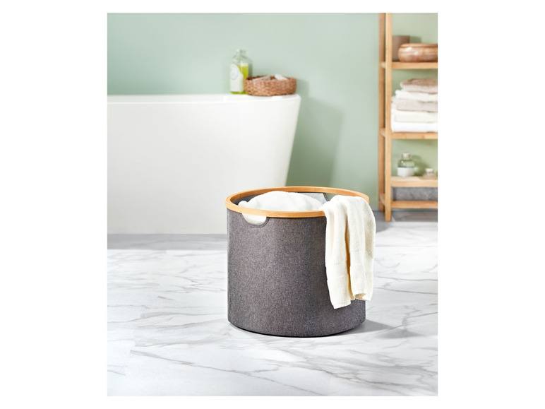 Ein grauer Wäschekorb mit Holzrand in einem Badezimmer.