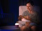 Eine Mutter füttert ihr Baby in einem dunklen Zimmer mit einer Nachtlampe mit einer Flasche.