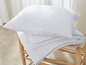 Ein weißes Kissen und eine weiße Bettdecke auf einem Holzhocker.