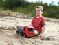 Ein Junge spielt mit einem roten LKW im Sand.