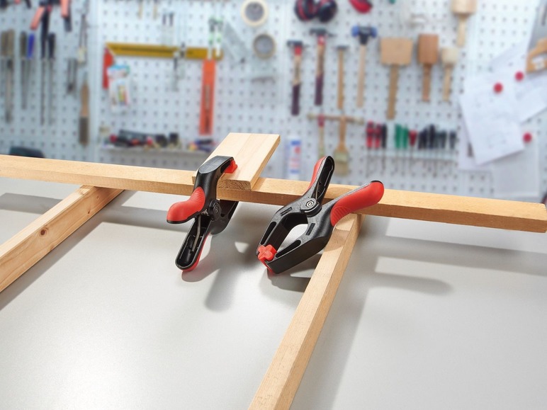 Zwei schwarze Klemmen mit roten Griffen, befestigt an Holz