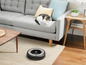Ein Roomba-Roboterstaubsauger auf einem Teppich in einem Wohnzimmer.