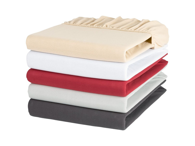 Stapel Bettwäsche in verschiedenen Farben, darunter Beige, Weiß, Rot, Grau und Dunkelgrau.