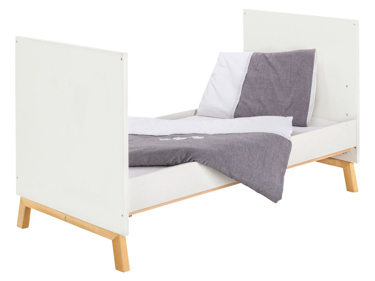 Weißes Kinderbett mit Holzbeinen und grauer Bettwäsche.