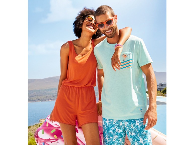 Eine Frau in einem orangefarbenen Jumpsuit und ein Mann in einem hellblauen T-Shirt mit Palmenprint und Badehose mit Palmenprint.