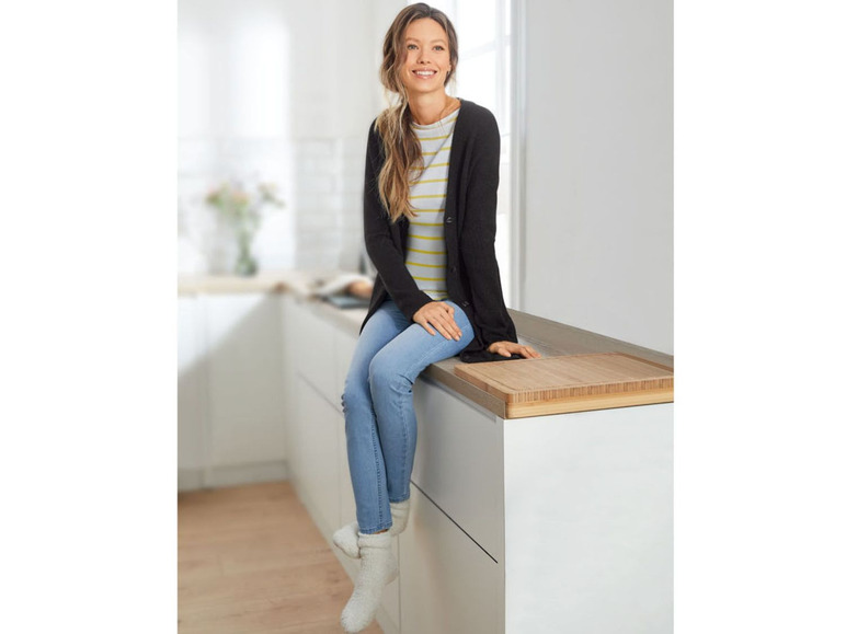 Eine Frau in einem schwarzen Pullover und blauen Jeans sitzt auf einer Küchenarbeitsplatte mit einem Holzbrett.