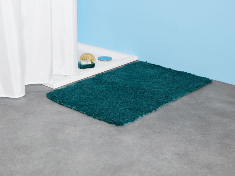 Ein dunkelgrüner Badezimmerteppich auf dem Boden.