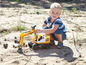 Ein Junge spielt mit einem gelben Liebherr-Bagger im Sand.