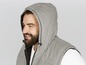 Ein Mann in einem grauen Kapuzenpullover und einer Weste.