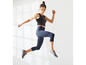 Frau in schwarzem Sport-BH und blauen Capri-Leggings springt.
