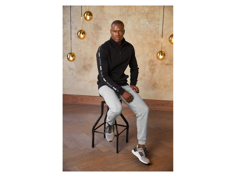 Mann trägt eine schwarze Kapuzenjacke und graue Jogginghose