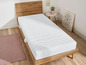 Eine weiße Matratze mit Wellensteppung auf einem Holzbettgestell.