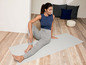 Frau in grauen Jogginghosen und blauem Oberteil auf einer Yogamatte.