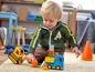 Ein Junge spielt mit Lego-Baufahrzeugen, darunter ein gelber Bagger und ein blauer LKW.