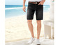 Mann trägt schwarze Jeans-Shorts mit weißen Sneakers am Strand.