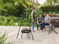Eine Gruppe von Menschen genießt ein Barbecue im Garten mit einem Dreibein und einem Grill.