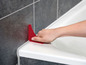 Eine Hand verwendet einen roten Silikon-Fugenzieher, um eine Badewanne abzudichten.