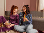 Zwei Frauen in Pyjamas mit Popcorn und einem Getränk.