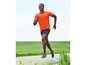 Mann in orangefarbenem T-Shirt und blauen Shorts beim Laufen im Freien.