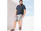 Mann in blauem Polo-Shirt, grauen Shorts und Sandalen.