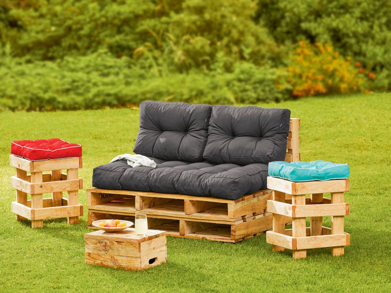 Eine Palettencouch mit Kissen, zwei Beistelltische und Stühle im Garten.