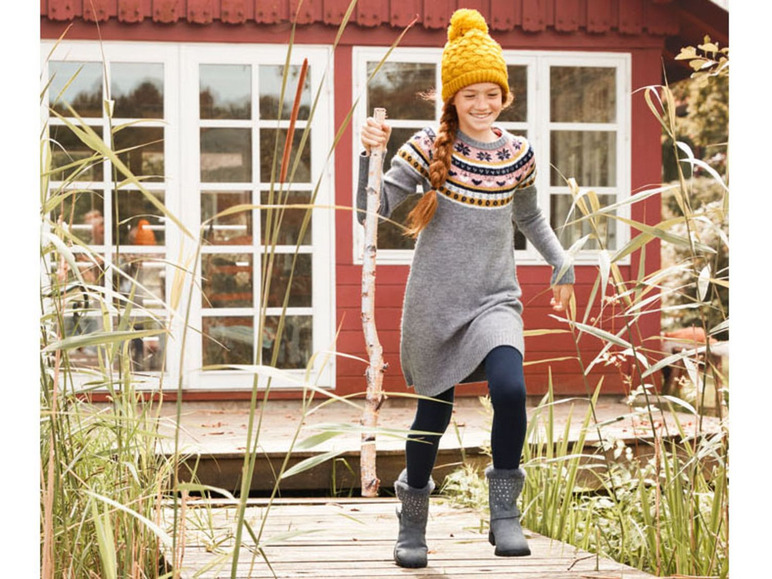 Ein Mädchen trägt einen grauen Pullover mit skandinavischem Muster, schwarze Leggings und graue Uggs.