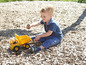 Ein kleiner Junge spielt mit einem gelben Spielzeug-LKW auf Holzspänen.