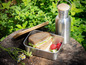 Ein Sandwich in einer Lunchbox aus Metall, ein Holzbrett und eine Edelstahl-Wasserflasche.