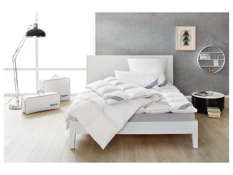 Schlafzimmer mit weißem Bett, Daunendecke und Kissen sowie zwei Bettwäschetaschen.