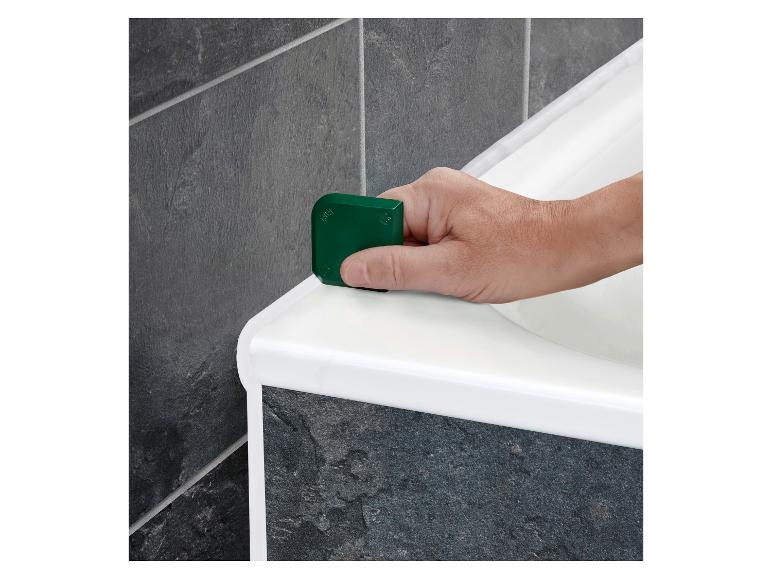 Hand glättet weiße Silikondichtung entlang einer Badewanne mit einem grünen Werkzeug.