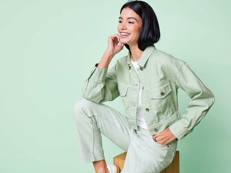Eine Frau in einer grünen Jeansjacke und -hose, lächelt.