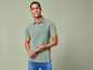 Mann in einem grünen Poloshirt und blauen Jeans.