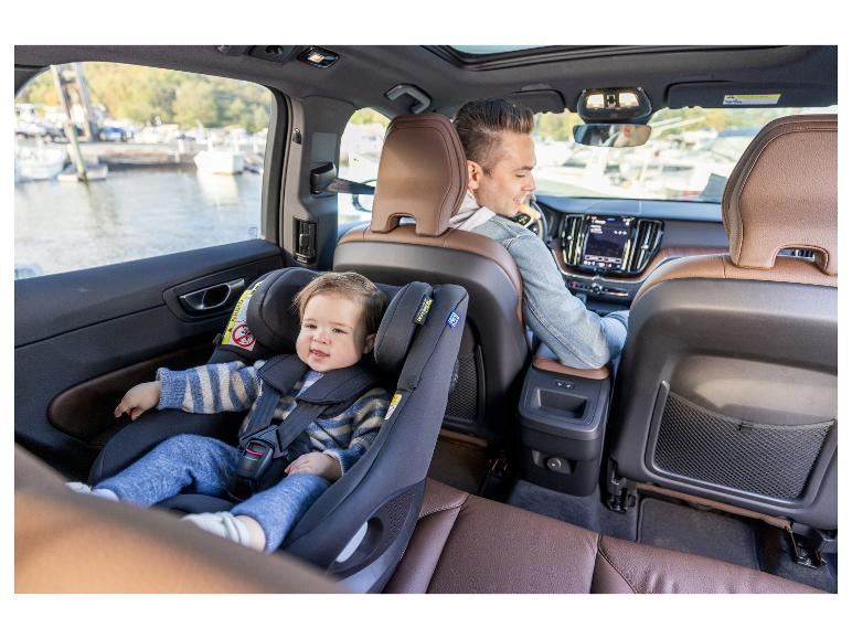 Baby im Kindersitz schaut nach vorne, ein Erwachsener fährt Auto.